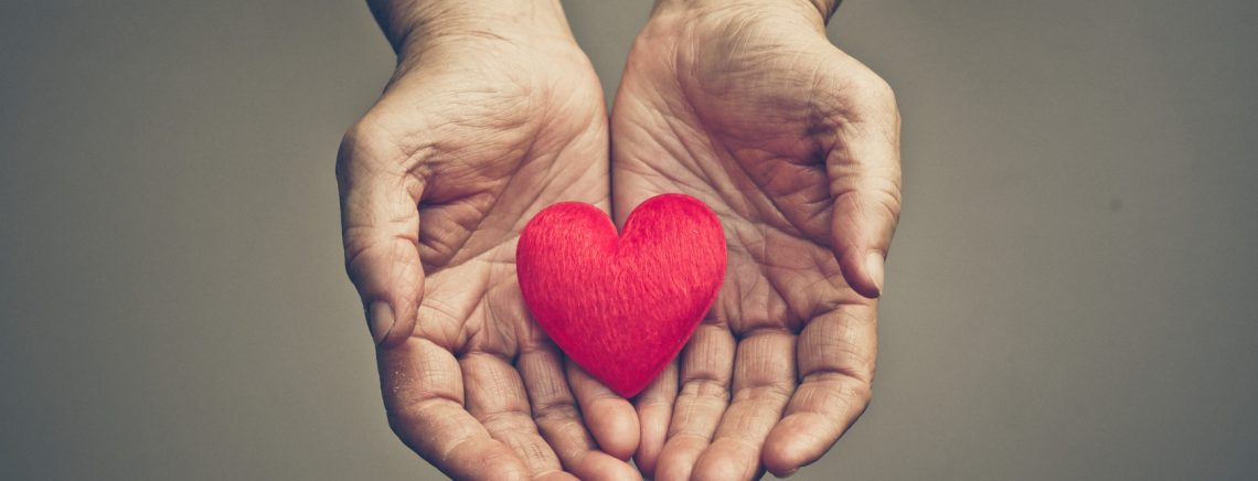 old hands of the elderly giving a red heart