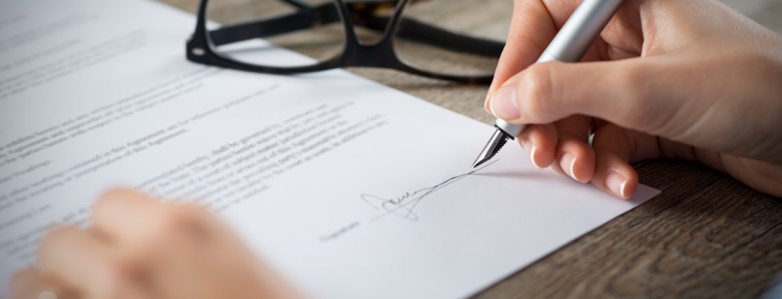 Closeup shot of a woman signing a form. She's writing on a financial contract. Shallow depth of field with focus on tip of the pen.